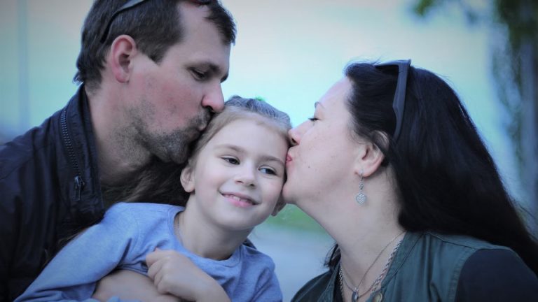 A heartwarming capture of parents showing love to their smiling daughter with gentle kisses.